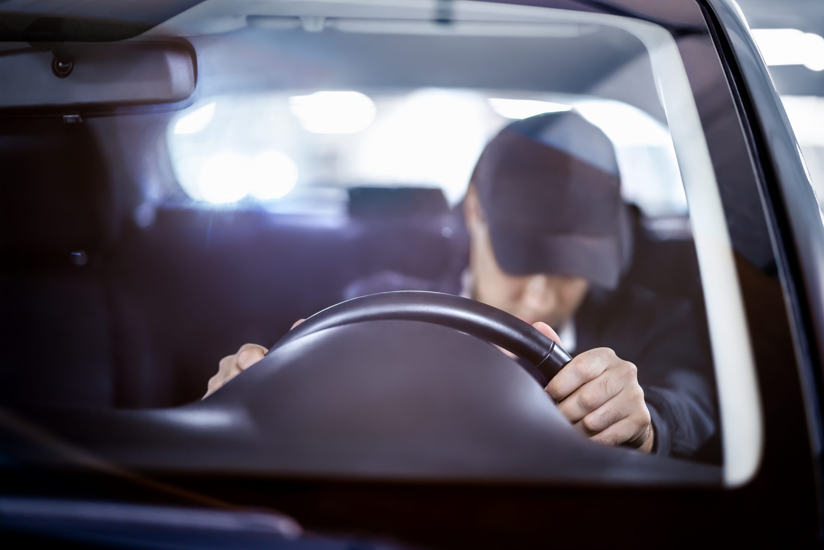 Homem de boné dentro do carro com a cabeça baixa    