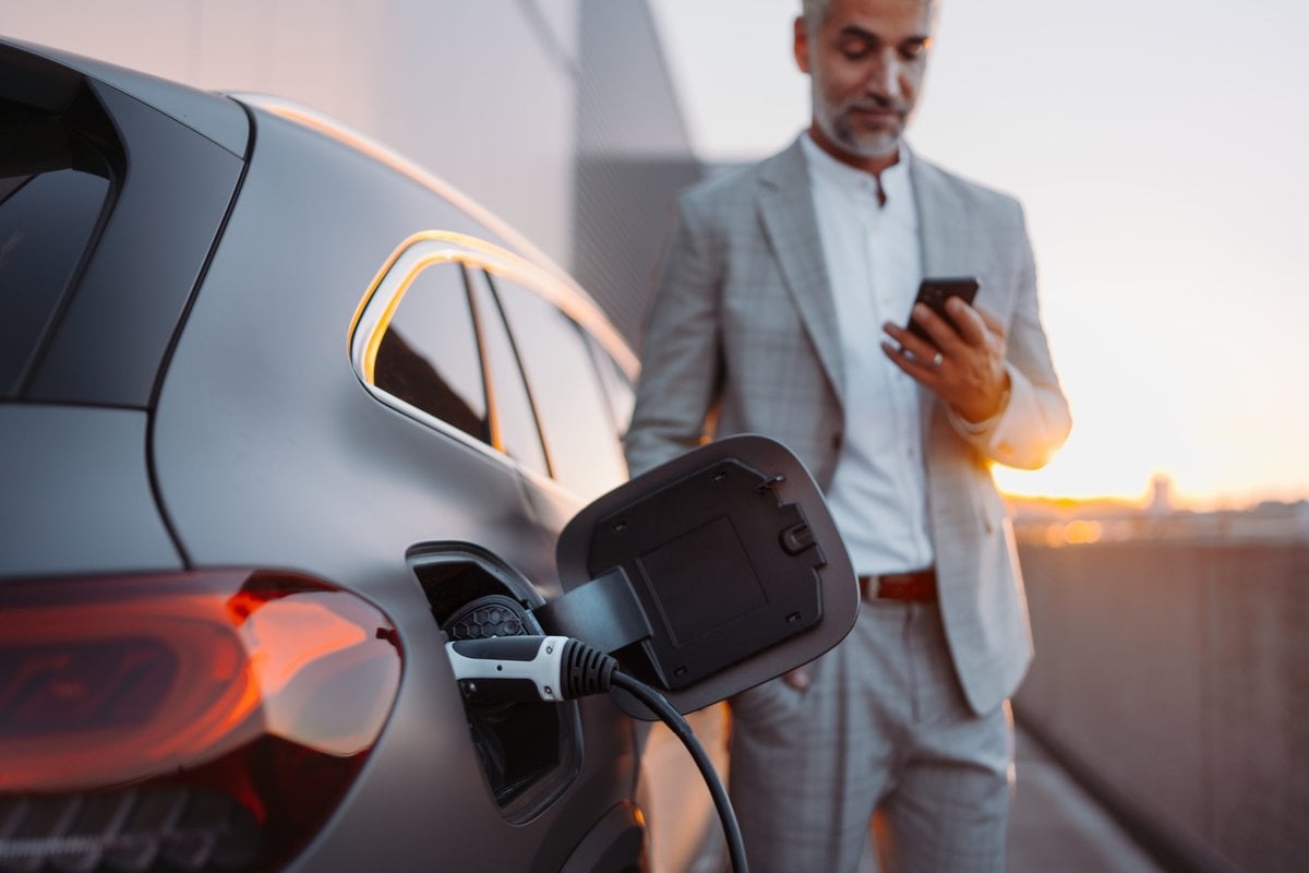 Homem mexendo no celular enquanto seu carro elétrico carrega     