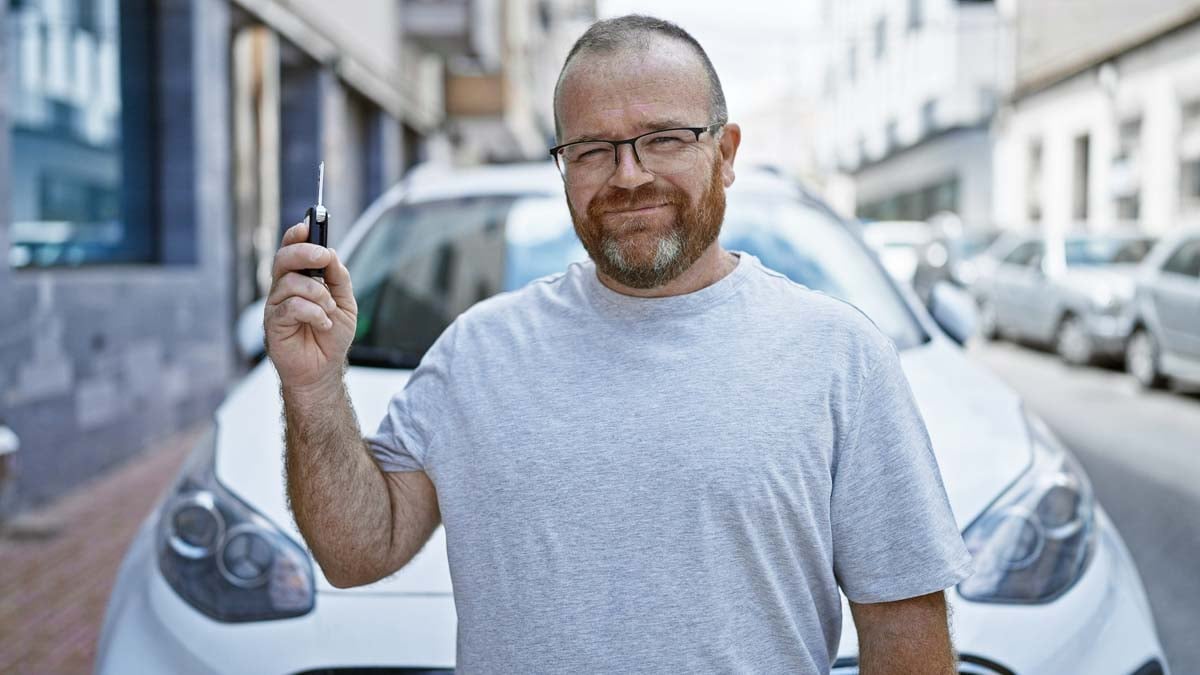 Homem em frente ao carro dele segurando a chave em sinal de conquista 
