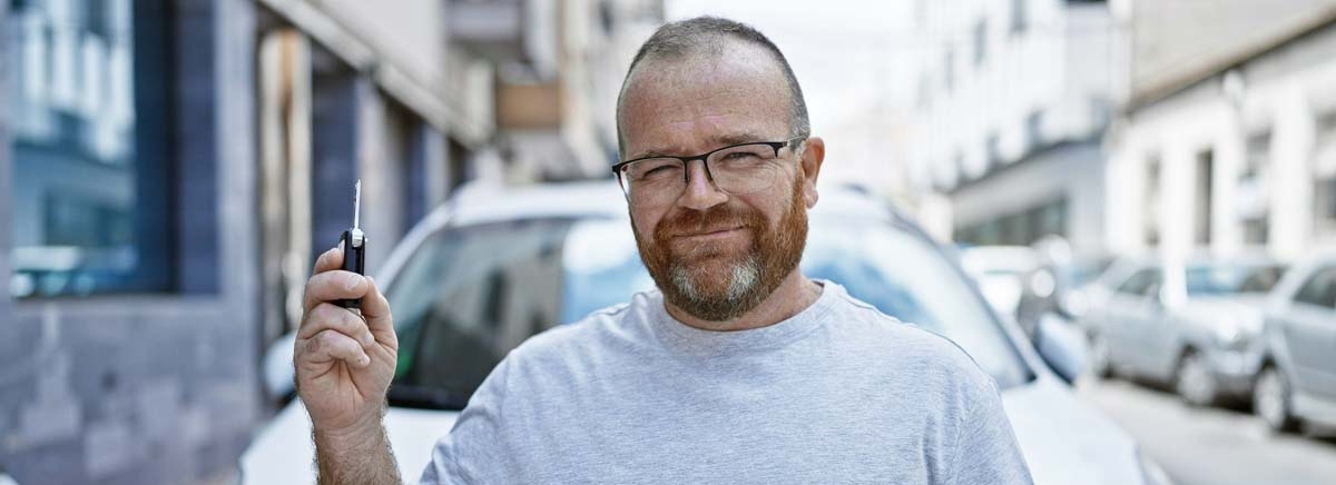 Homem em frente ao carro dele segurando a chave em sinal de conquista 