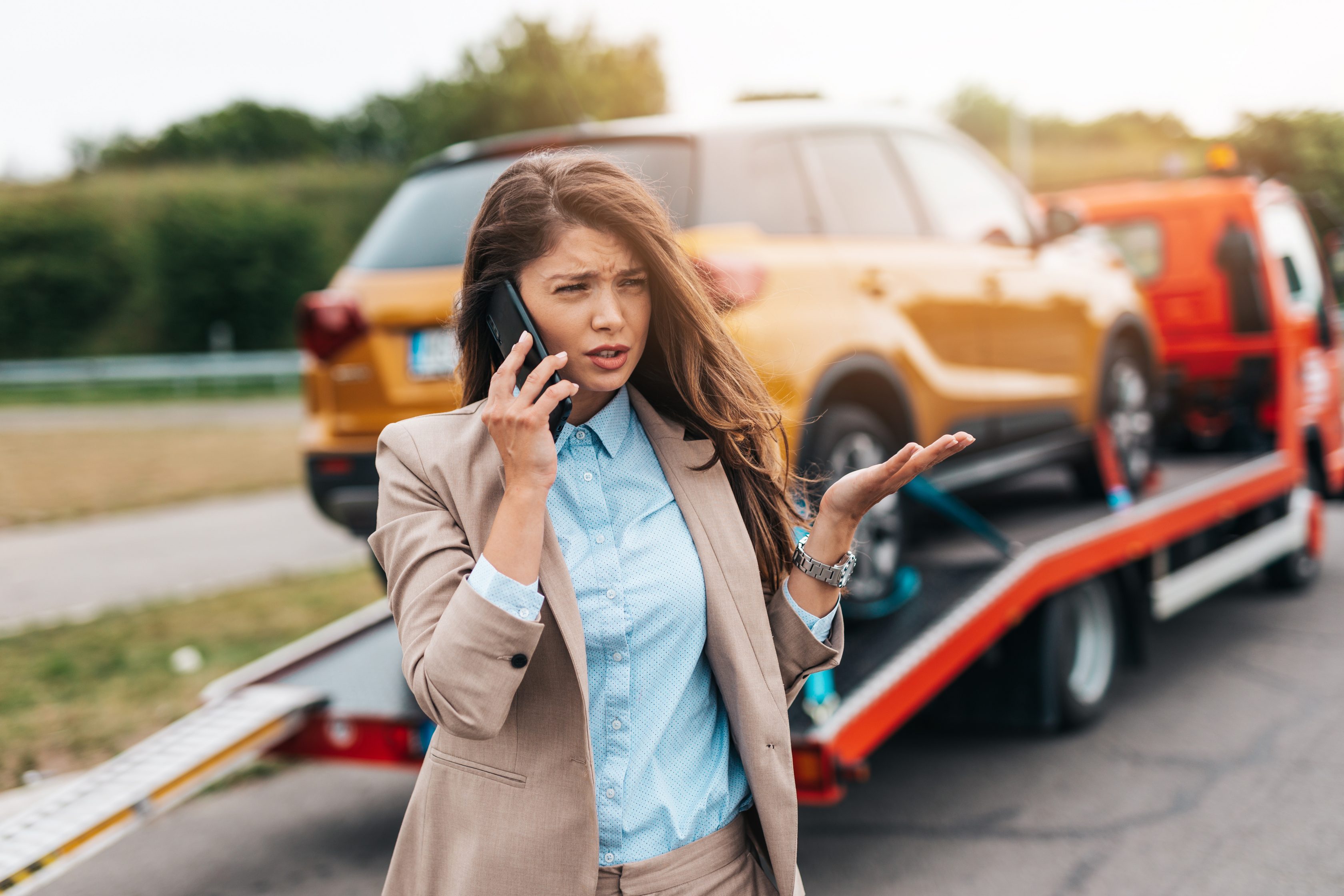Mulher falando ao telefone com carro sendo rebocado