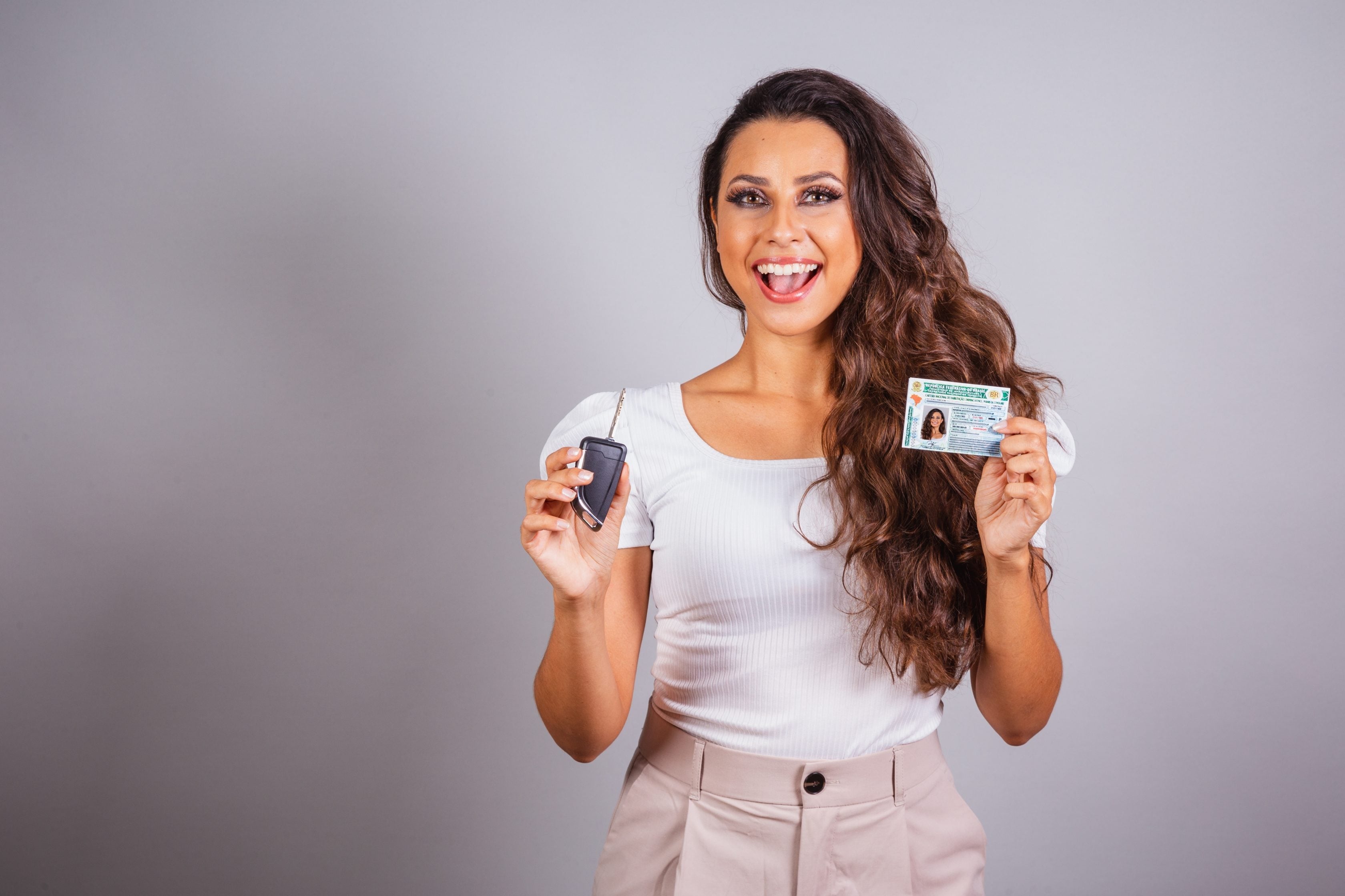 Mulher exibindo sua CNH e a chave de um veículo    