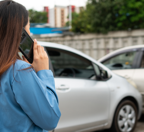 Imagem de veículo que colidiu com carro estacionado enquanto motorista entra em contato pelo celular com a seguradora