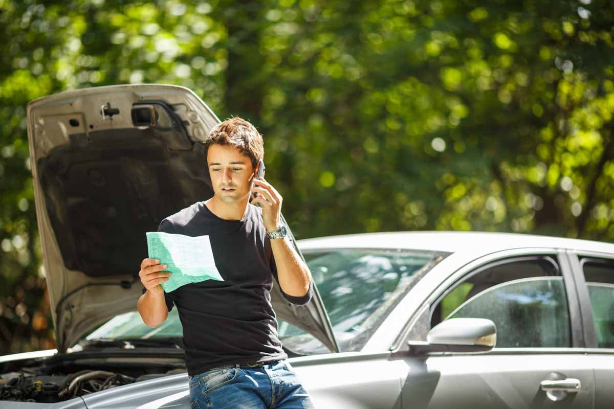Homem falando ao celular ao lado do carro quebrado     