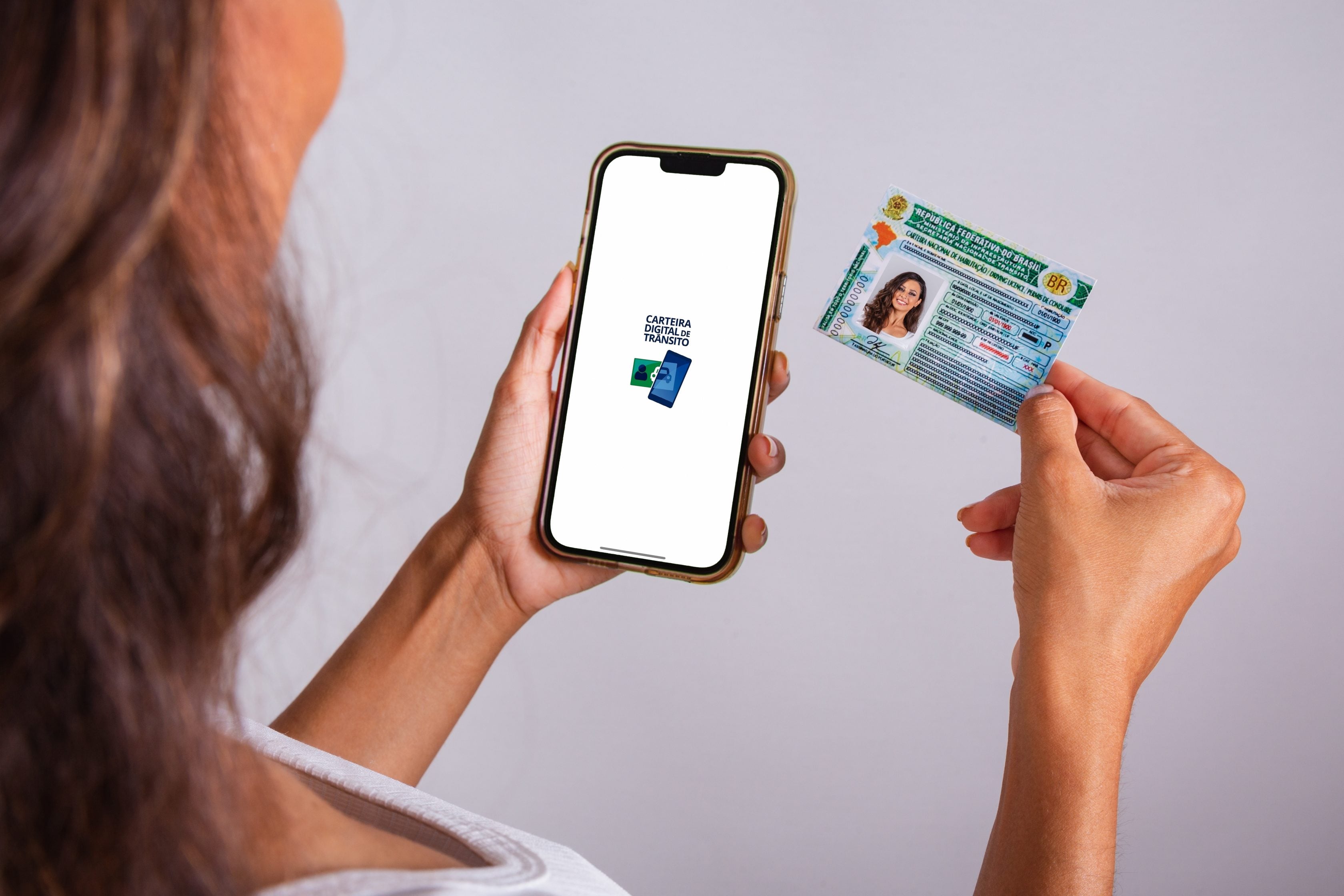 Mulher utilizando o celular e segurando sua CNH      