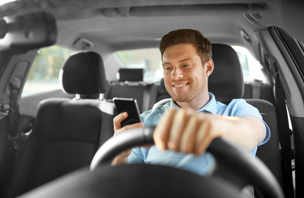 Homem dirigindo seu carro e utilizando o celular      