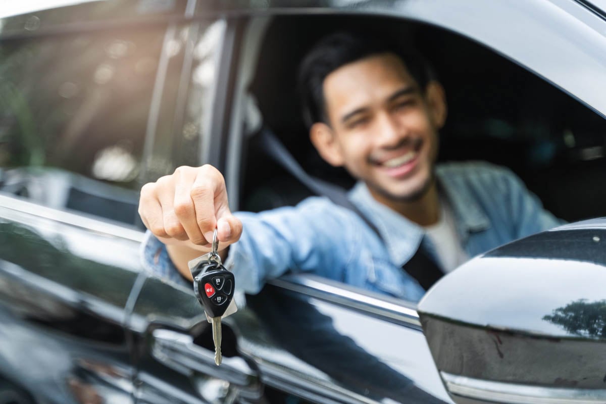 homem sorrindo segurando uma chave de carro pela janela do carro