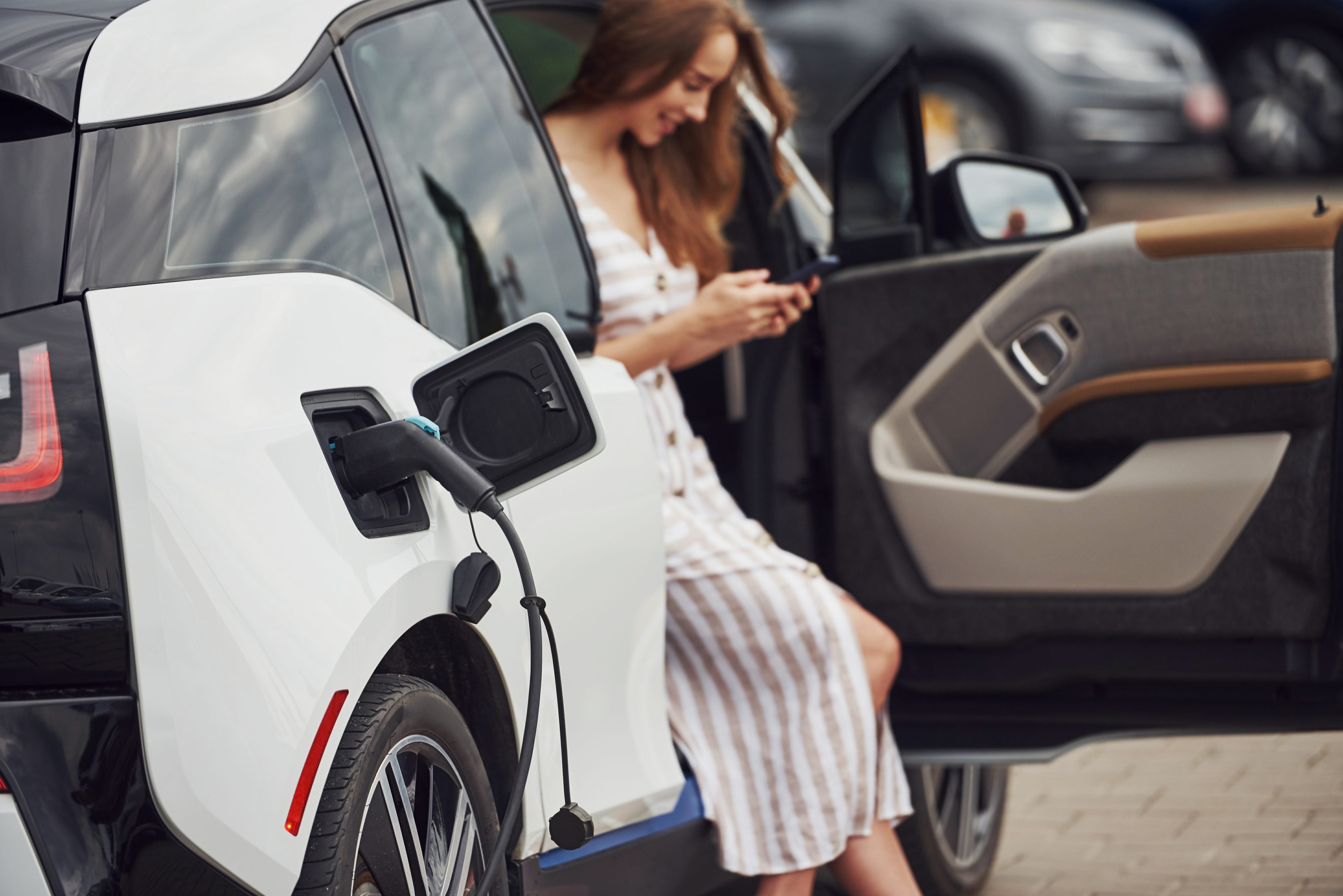 Mulher mexendo no celular enquanto seu veículo elétrico carrega     