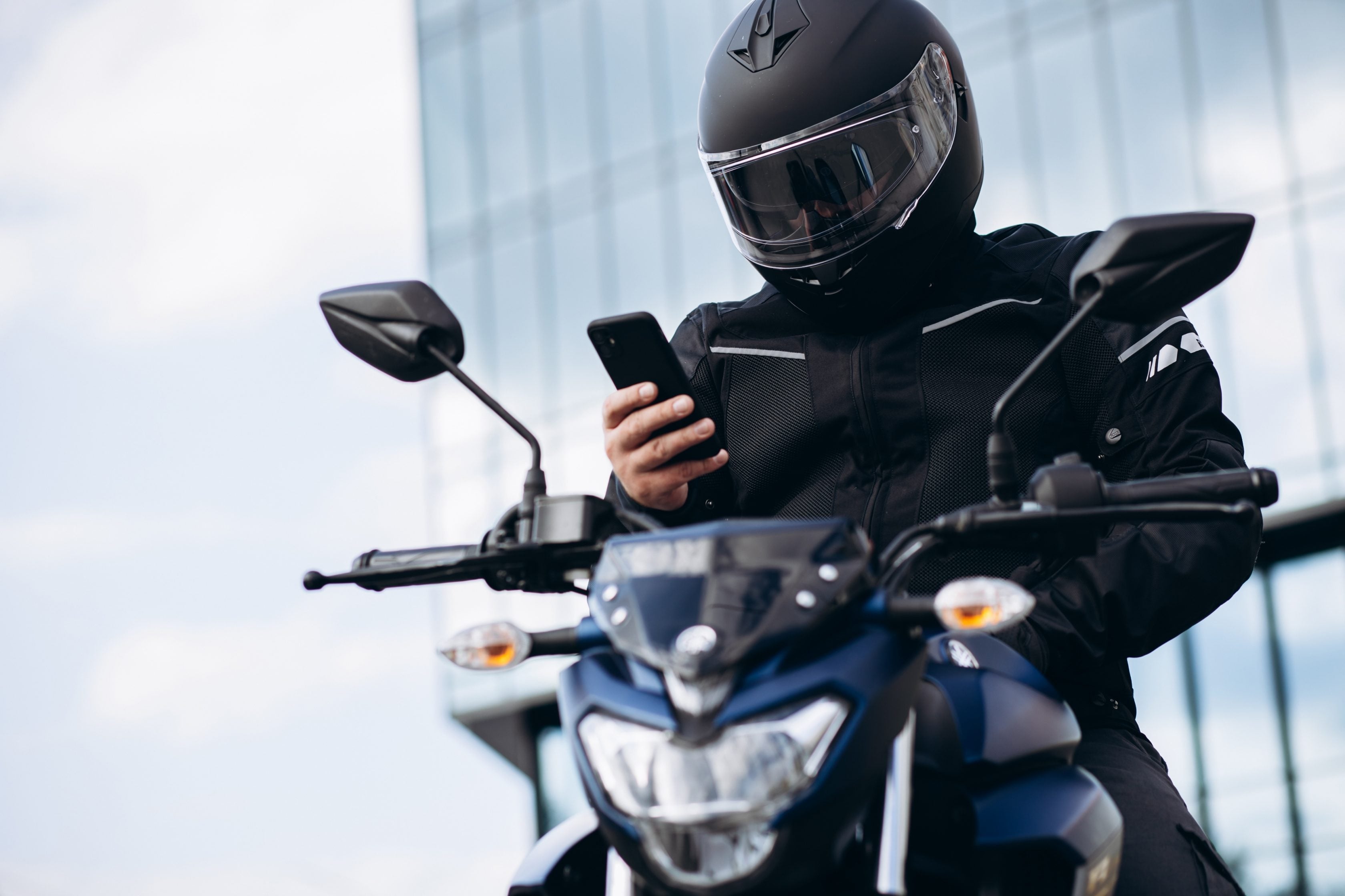 Motoqueiro mexendo no celular em cima de uma moto parada