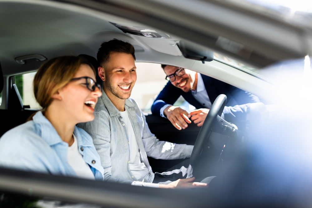 Casal e vendedor sorrindo dentro de um carro em uma concessionária