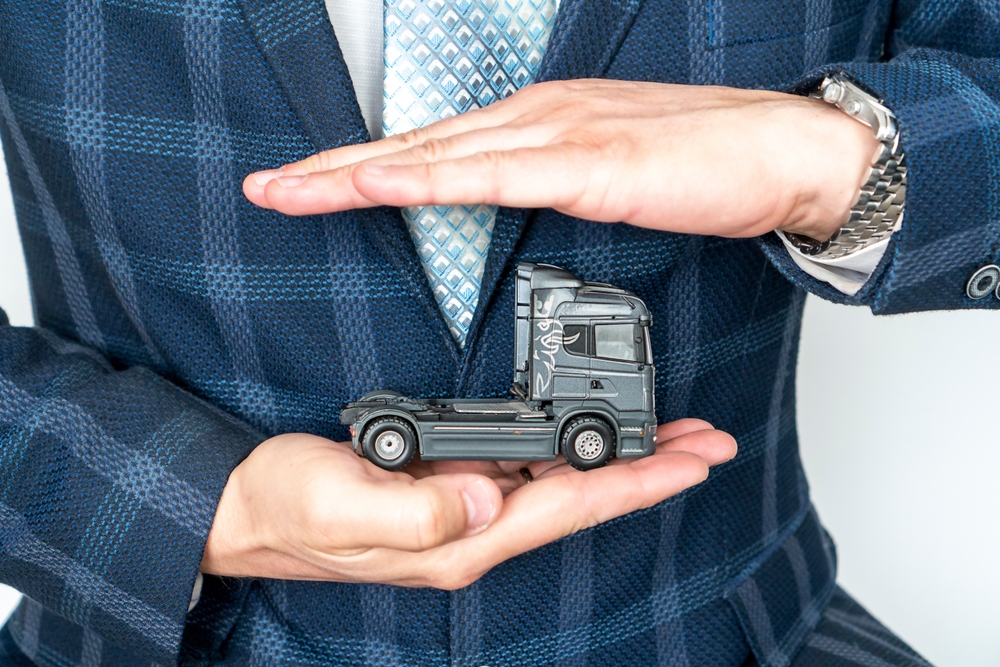 Homem de terno segurando uma miniatura de caminhão, representando o seguro caminhão