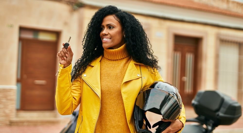 Mulher sorrindo com a chave de sua moto e o capacete em suas mãos