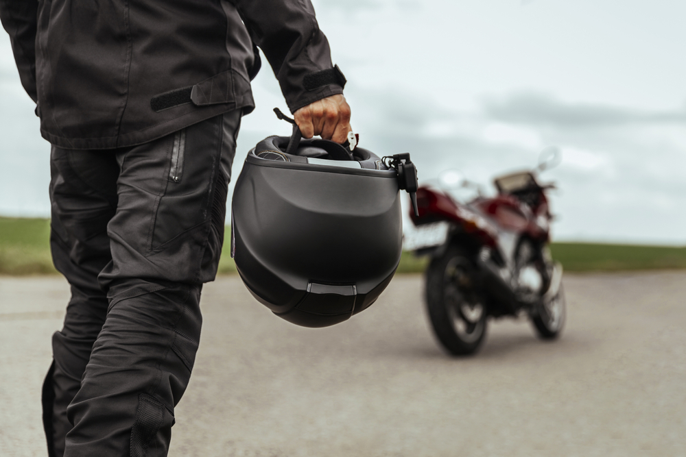 Homem segurando capacete atrás de sua moto