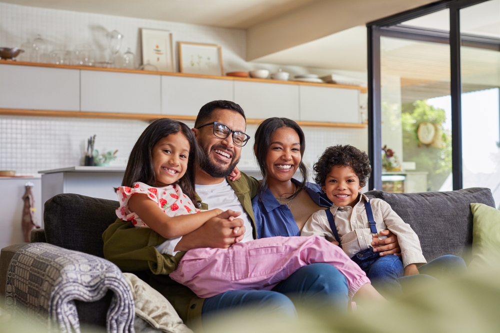 Família formada por pai, mãe e filhos sorrindo e sentados no sofá