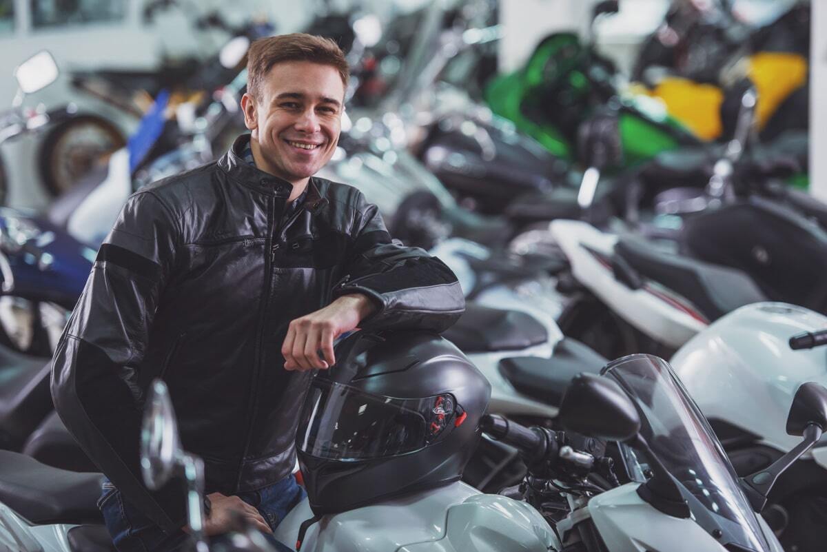 Homem próximo de uma moto sorrindo