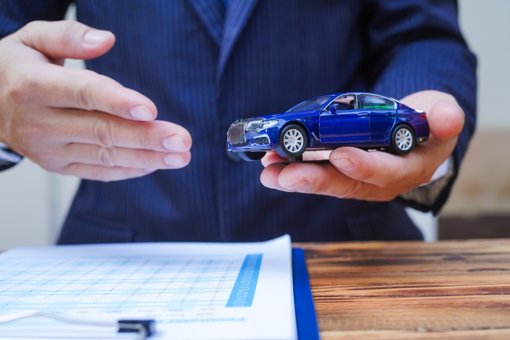 Corretor da Allianz segurando miniatura de carro azul, oferecendo Seguro Auto