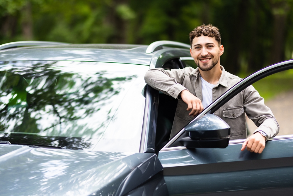 Homem sorrindo em pé ao lado de seu carro