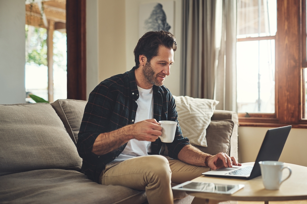 Homem sentado no sofá de sua casa usando o notebook