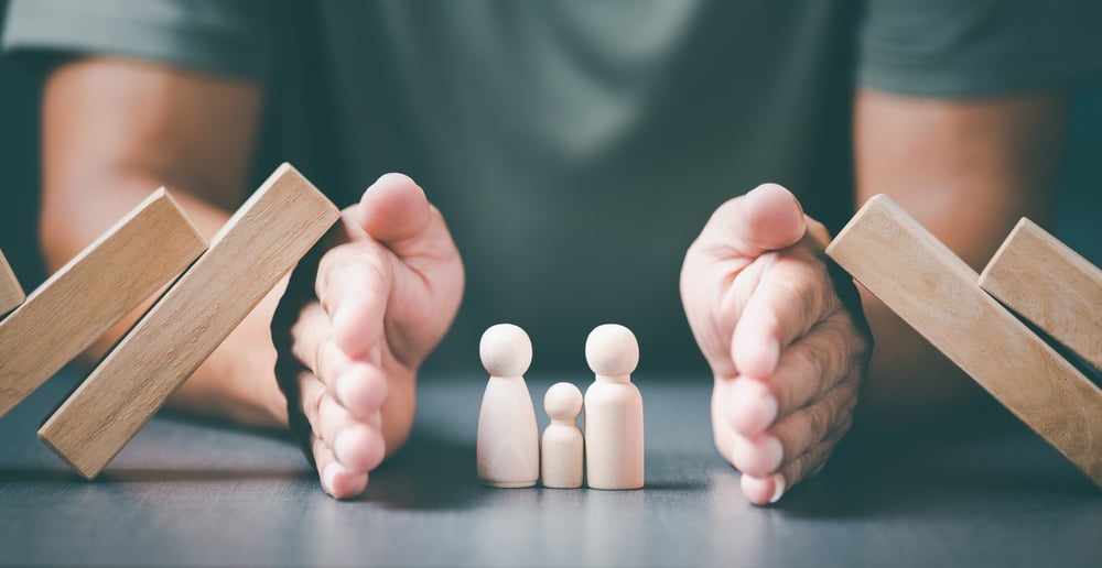 Homem protegendo bonecos de madeira com as mãos representando o seguro de vida
