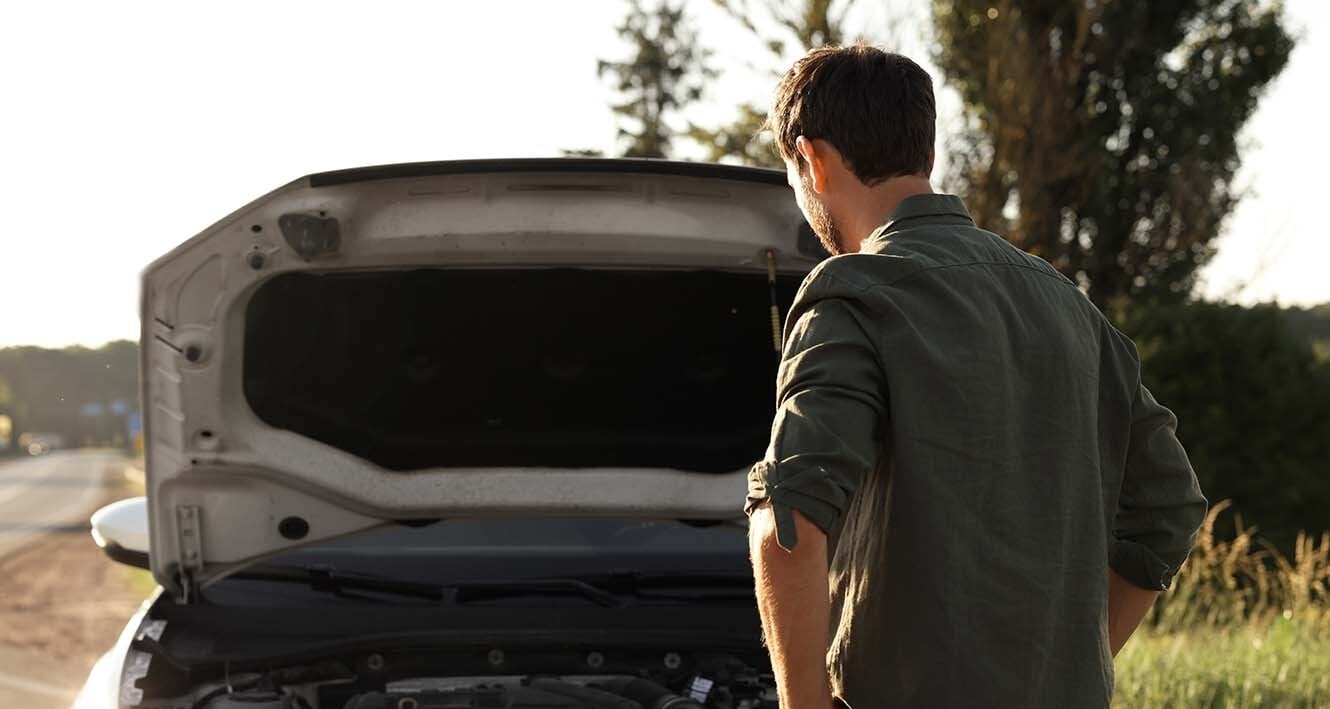 Homem em frente ao seu carro quebrado na estrada