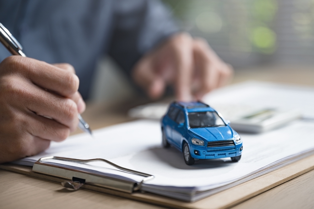 Imagem ilustrativa de pessoa assinando um documento e uma miniatura de carro que representam o seguro auto