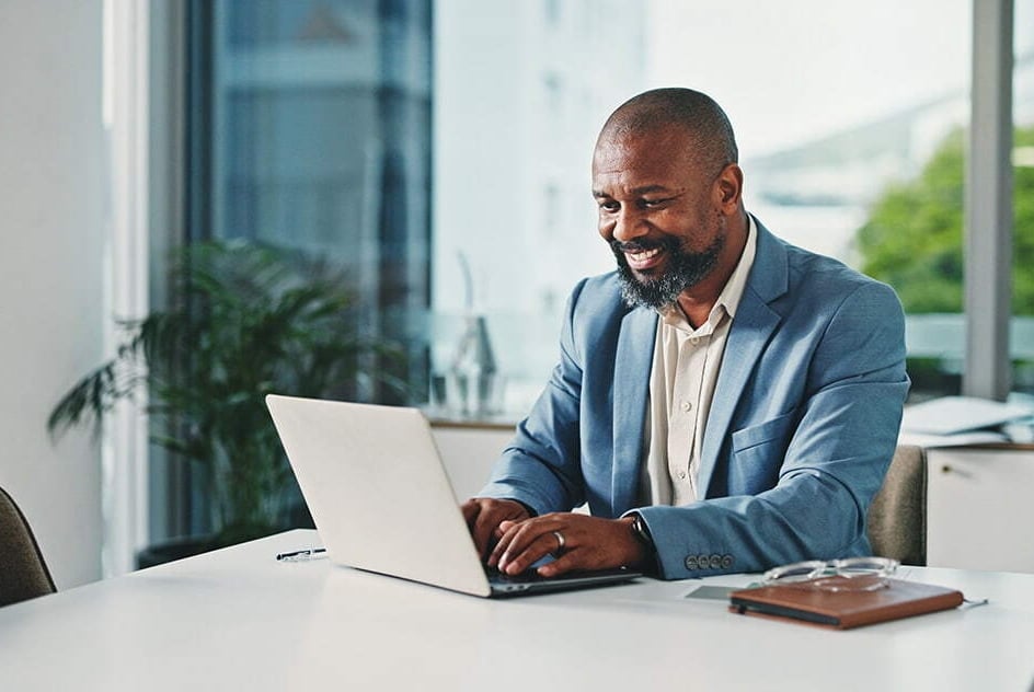 Homem trabalhando no escritório, usando notebook e sorrindo