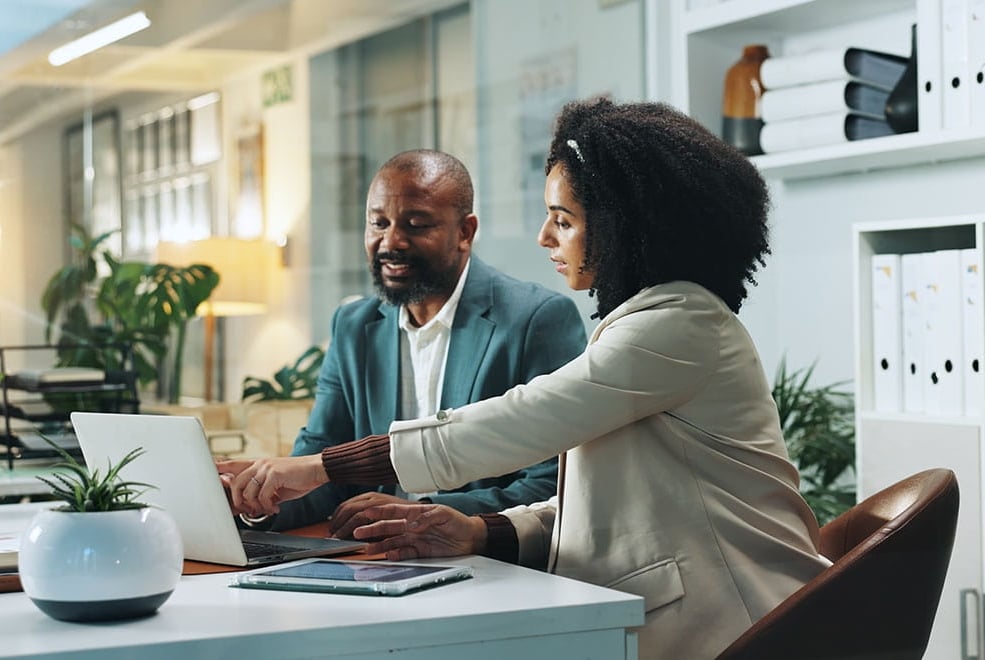 Homem e mulher sentados e conversando em mesa de escritório