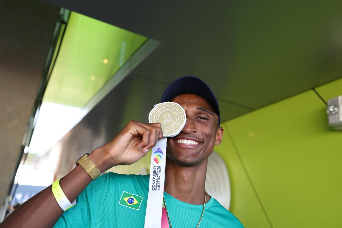 Atleta Alison dos Santos segurando medalha próximo ao rosto