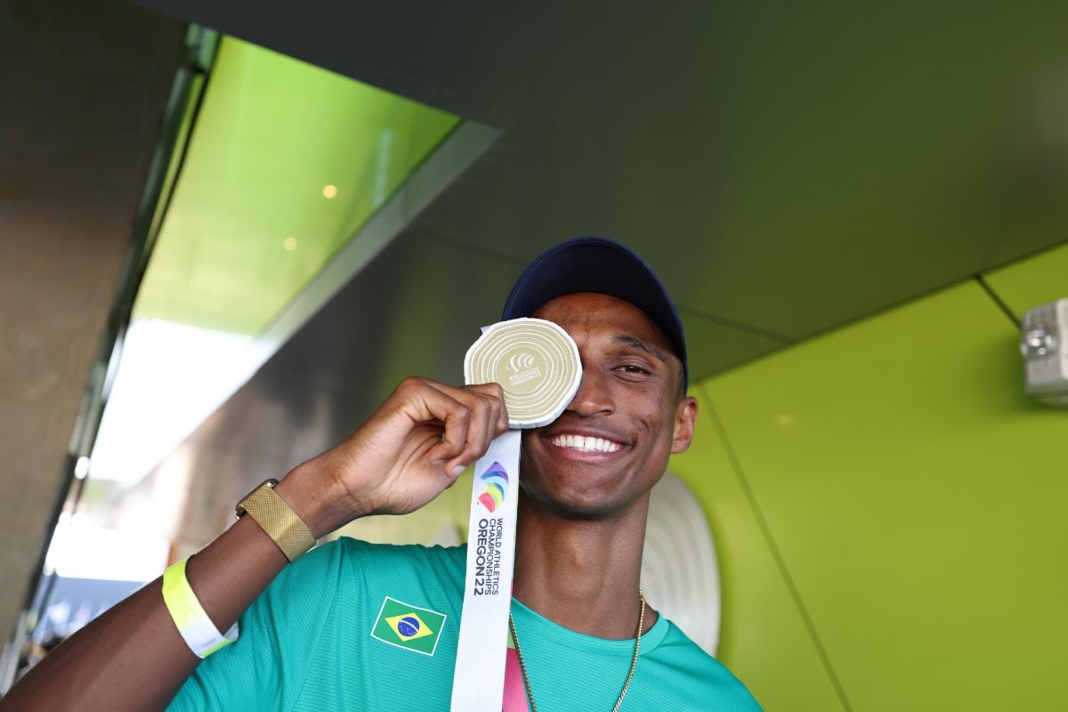 Atleta Alison dos Santos segurando medalha próximo ao rosto