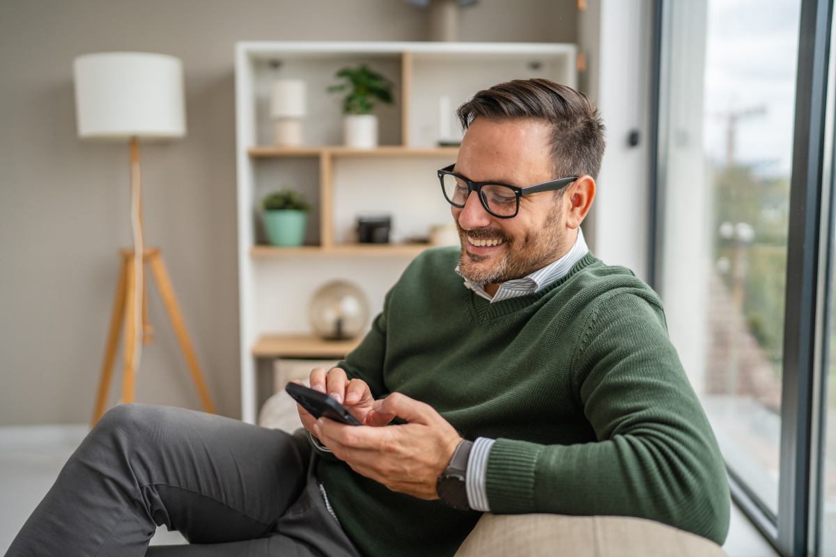 Homem sentado, usando o celular e sorrindo
