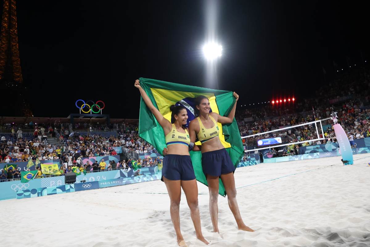 Atletas Duda e Ana Patrícia segurando bandeira do Brasil em quadra de areia nas Olimpíadas de Paris