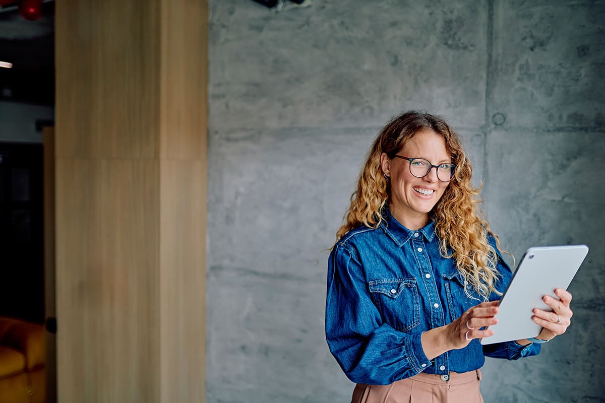 Mulher sorrindo no escritório e segurando um tablet