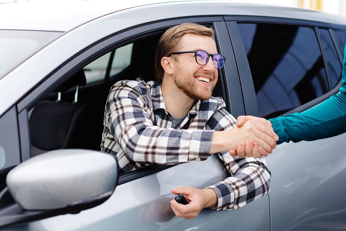 Homem apertando as mãos do vendedor após comprar um carro