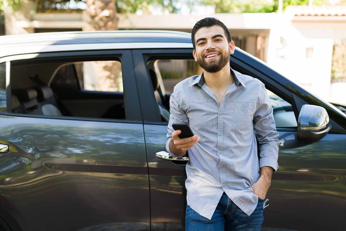 Homem feliz em frente a um carro segurando o celular