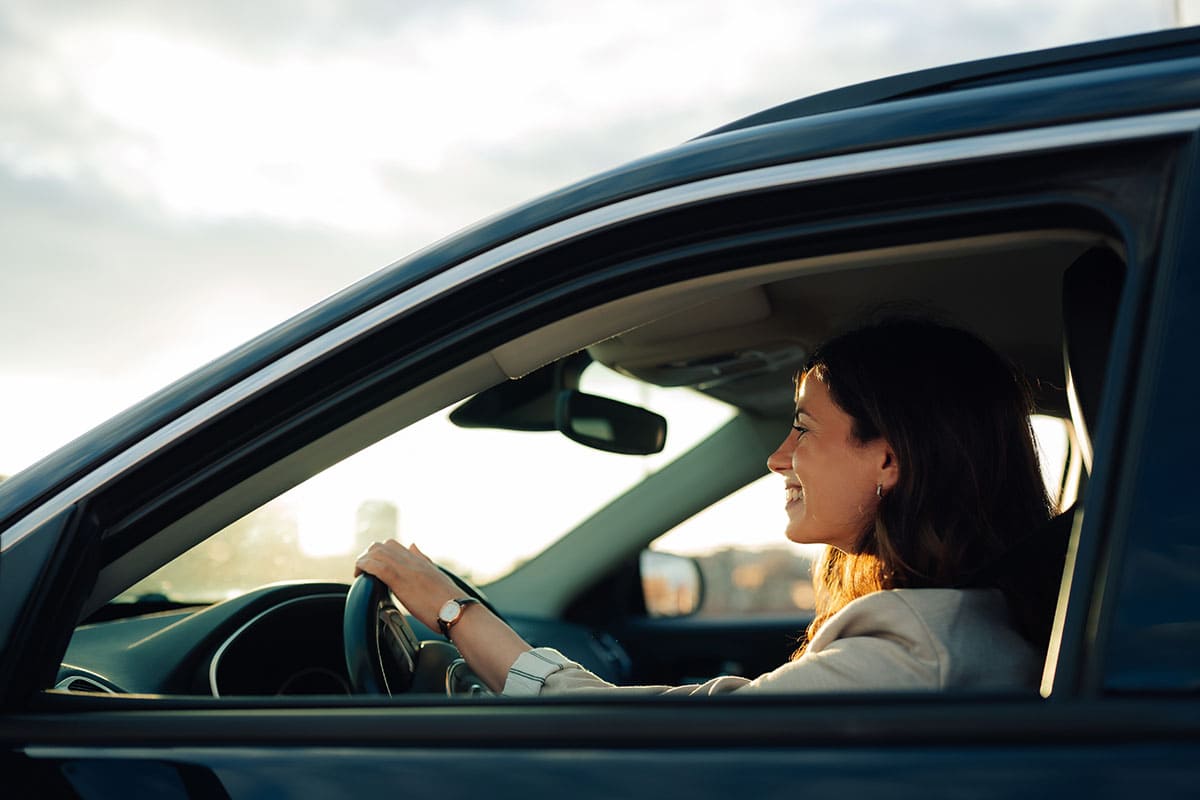 Mulher sorrindo e dirigindo seu carro