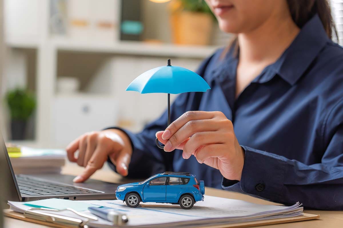 Mulher segurando um guarda-chuva em cima e uma miniatura de carro, representando o seguro auto