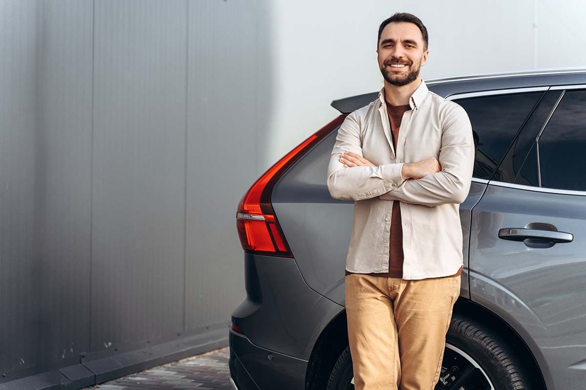Homem sorrindo e encostado no seu carro