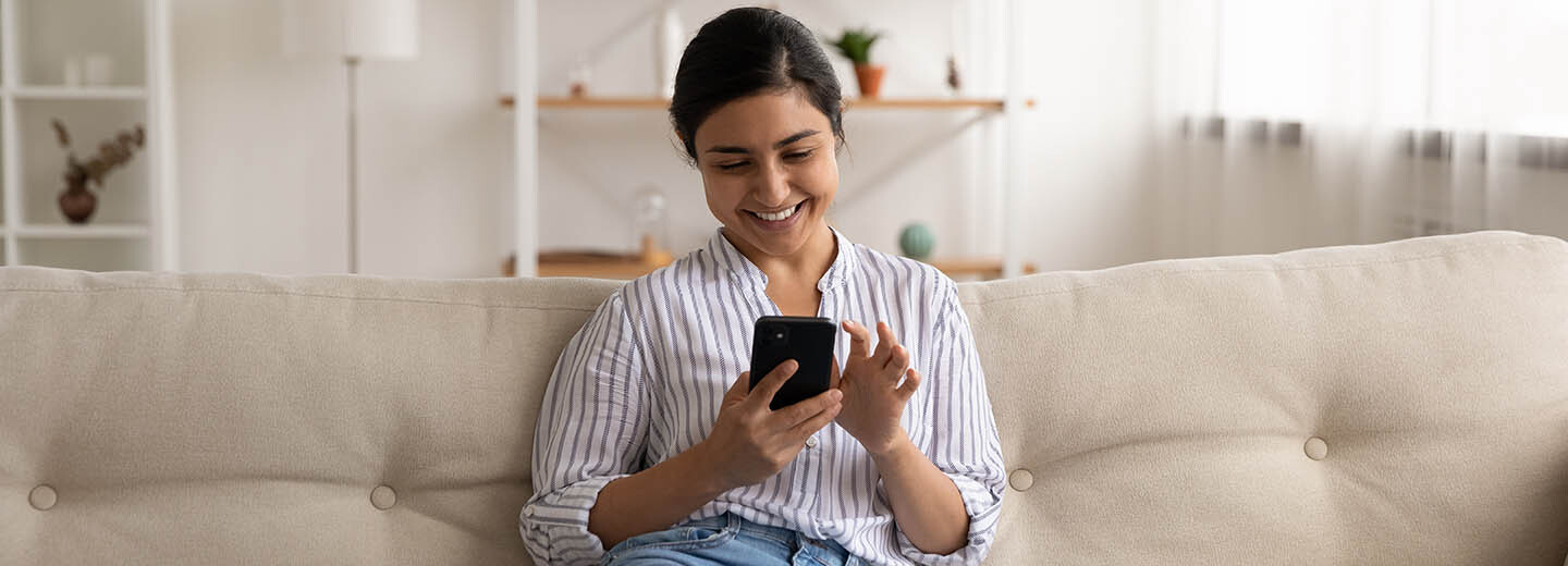 Mulher usando o celular sentada no sofá da sala