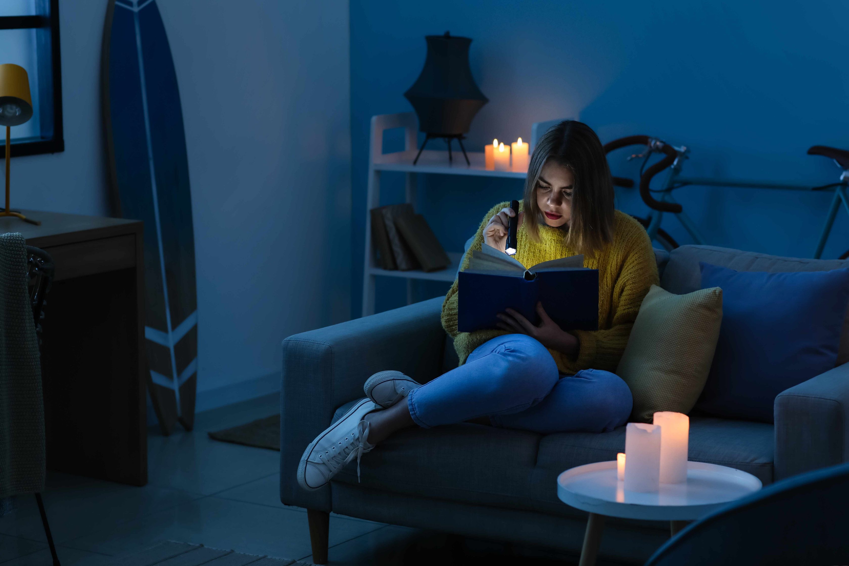 Mulher jovem lendo livro à luz de velas após falha elétrica
