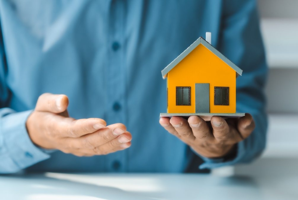 Homem com miniatura de casa na mão representando o seguro residencial