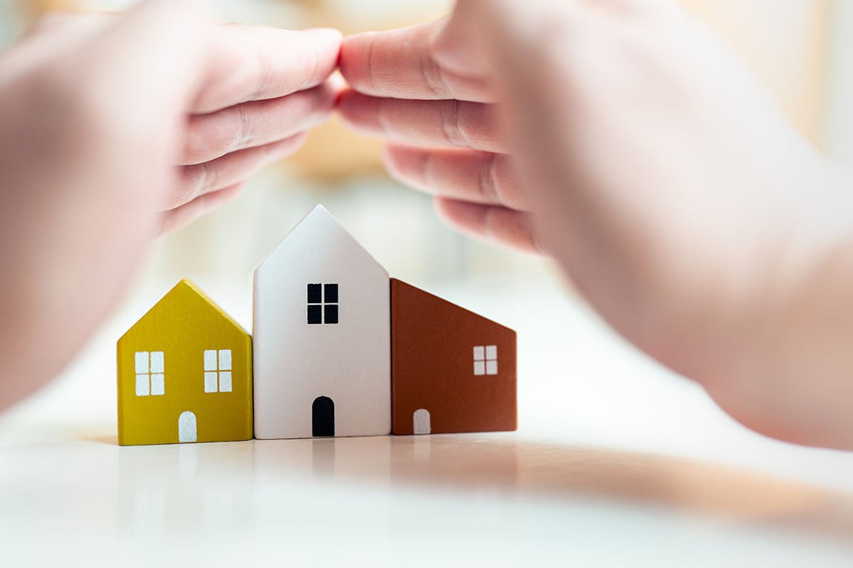 Mãos humanas em torno de uma miniatura de casa representando o seguro residencial