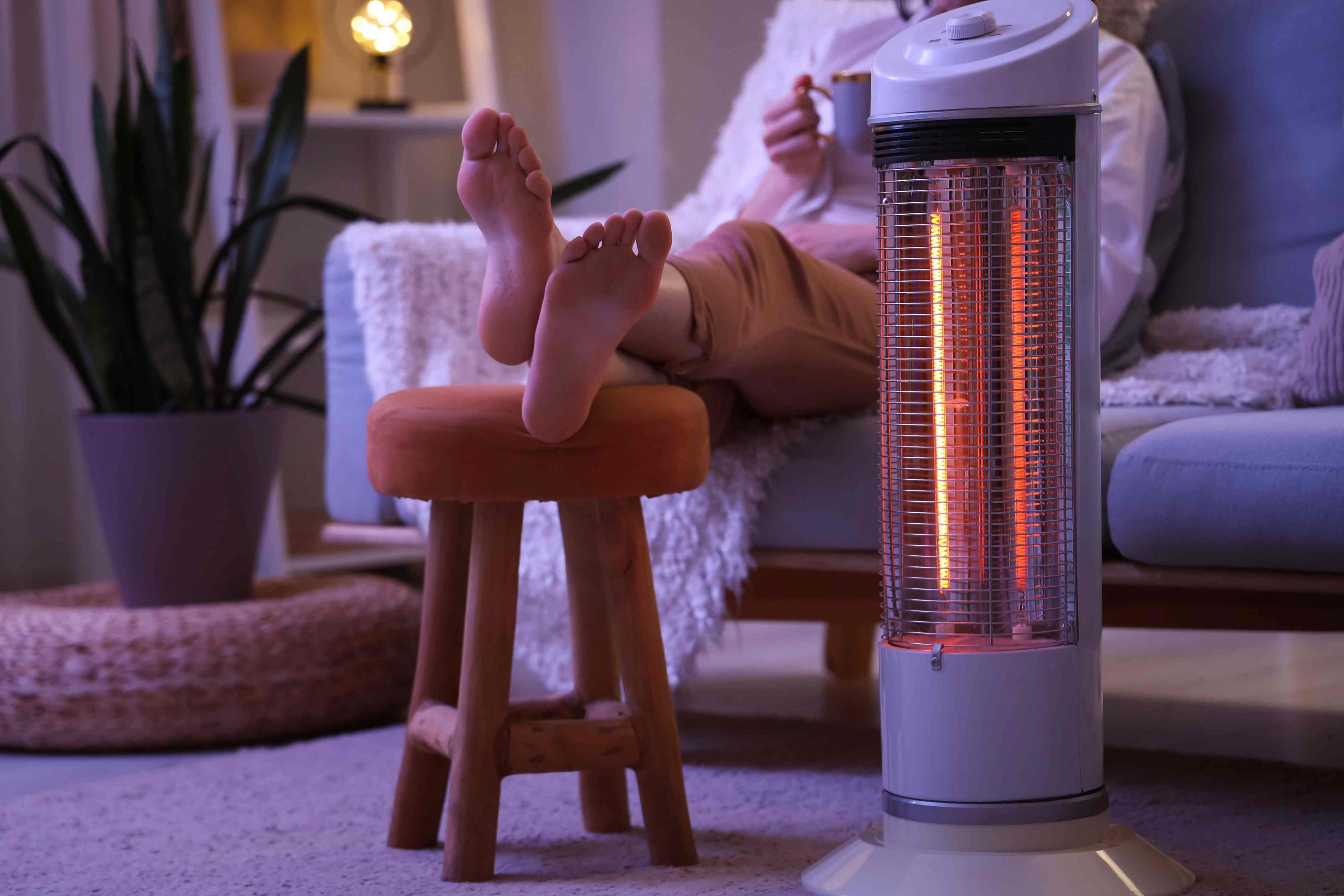 Mulher jovem sentada no sofá próxima a um aquecedor elétrico