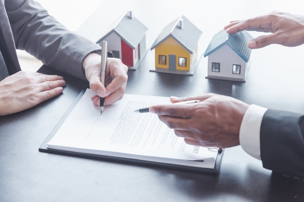 Homem assinando seguro residencial ao lado de três miniaturas de casas.