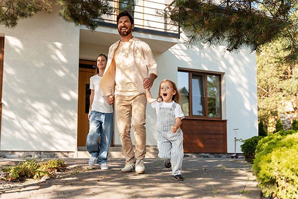 Família feliz de mãos dadas em frente à sua casa