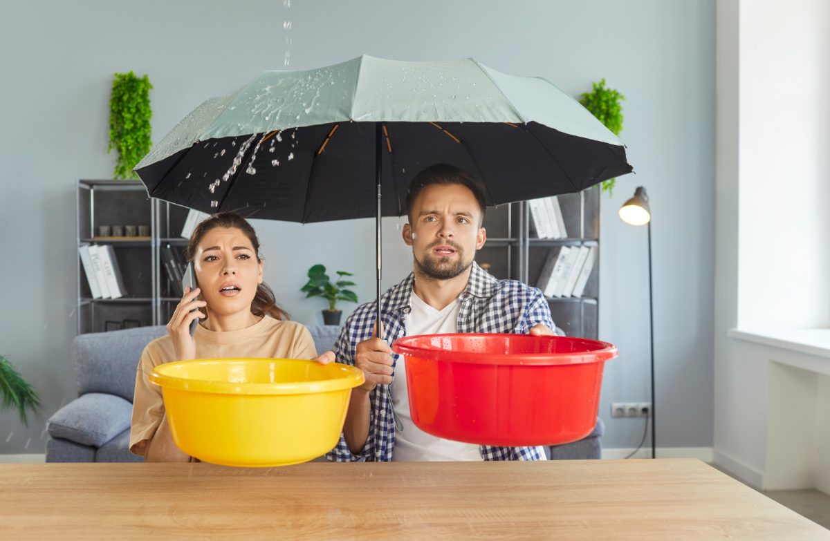 Casal dentro de casa com um guarda-chuva aberto e protegendo-se de um vazamento no teto