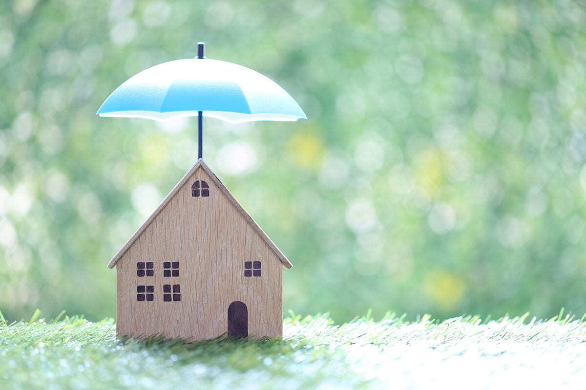 Miniatura de casa e guarda-chuva representando o seguro residencial