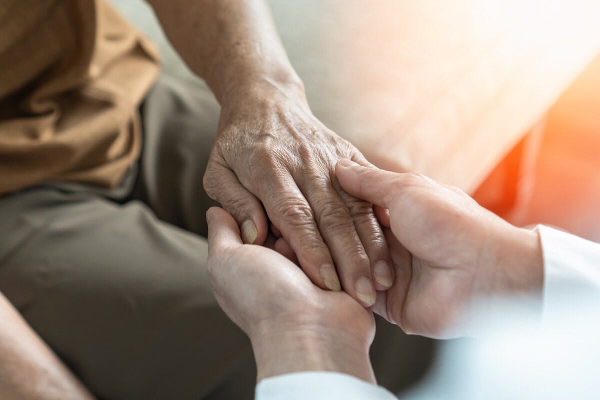 Mão de pessoa idosa sendo segurada pelas mãos de uma pessoa jovem
