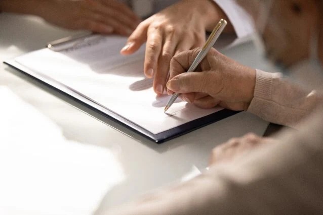  Close da mão de uma mulher idosa assinando um documento