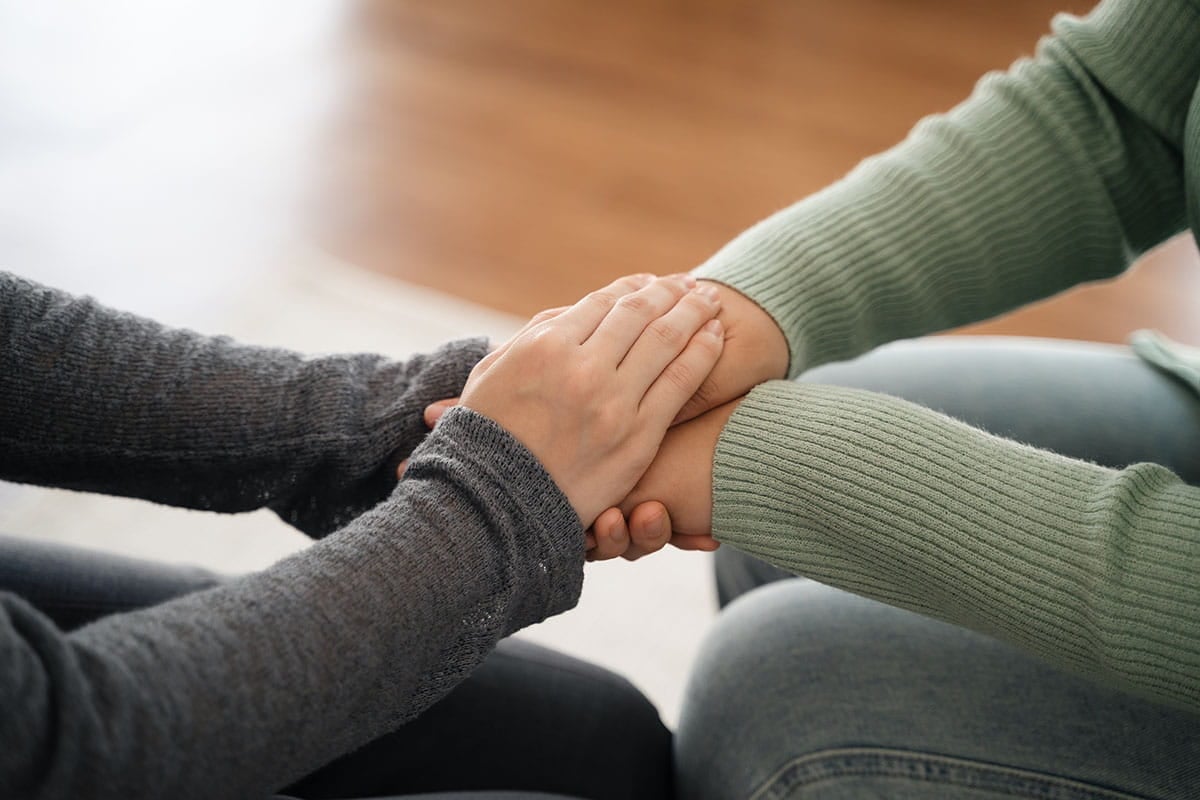 Duas pessoas de mãos dadas, confortando-se mutuamente