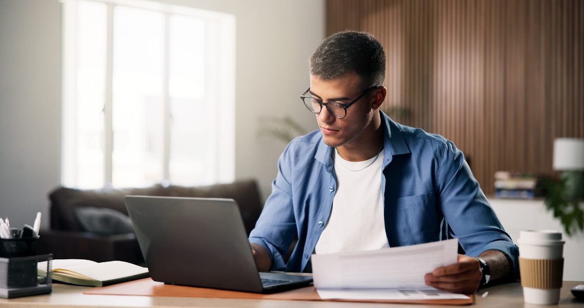 Homem usando notebook com papel nas mãos
